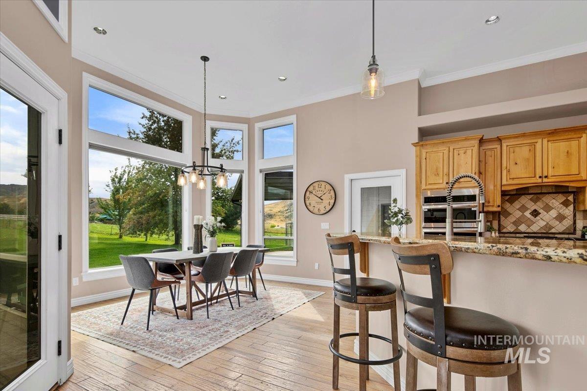 Kitchen with light stone countertops, decorative light fixtures, plenty of natural light, ornamental molding, and tasteful backsplash.