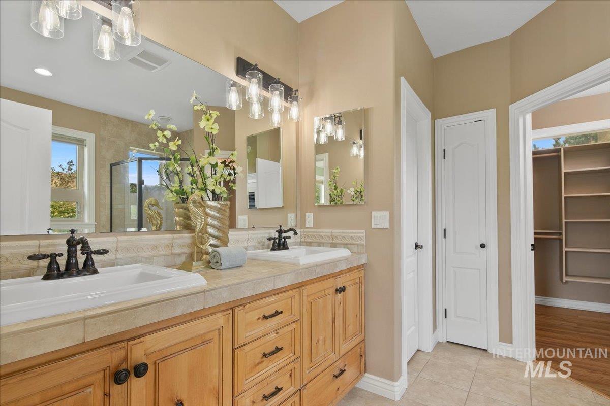 Full bath with healthy amount of natural light, double vanity, light tile patterned floors, and a stall shower