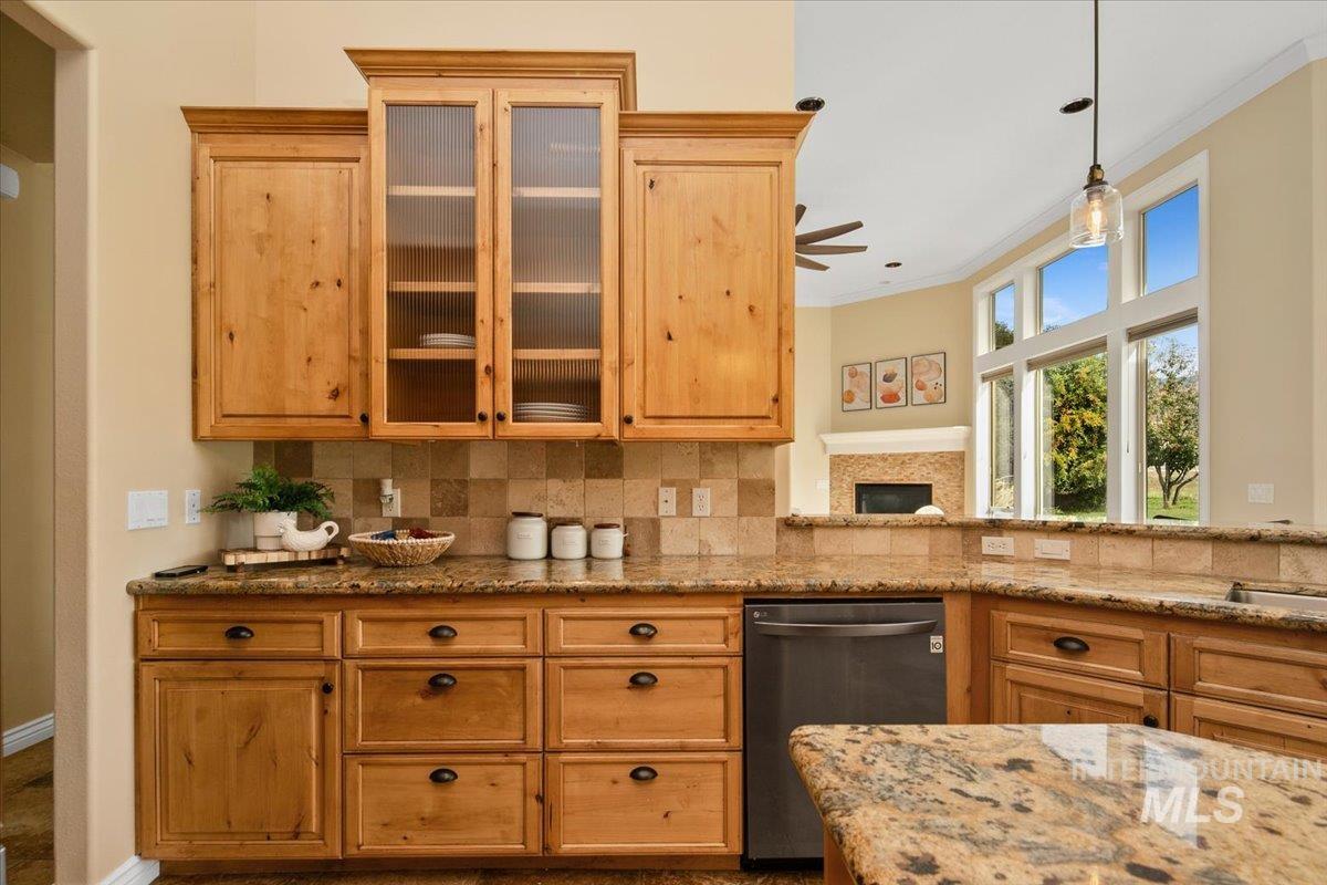 Kitchen with tasteful backsplash, glass insert cabinets, dishwasher, light stone counters, and ornamental molding