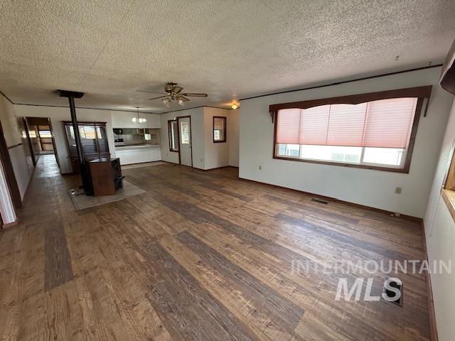 Unfurnished living room featuring a wood stove, dark wood finished floors, a textured ceiling, and ceiling fan