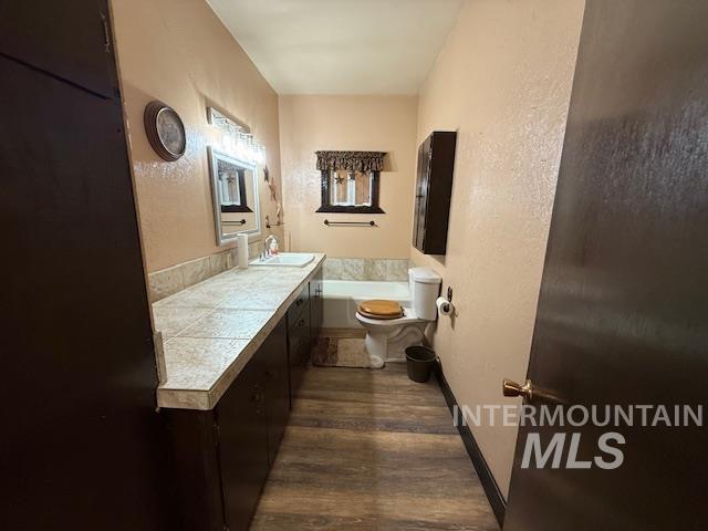 Full bath featuring a textured wall, dark wood-type flooring, vanity, and a garden tub