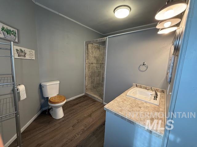 Full bath with dark wood-type flooring, vanity, ornamental molding, and tiled shower