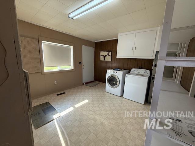 Washroom with cabinet space, light floors, wooden walls, and independent washer and dryer
