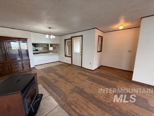 Unfurnished living room with a textured ceiling, a chandelier, a wood stove, tile patterned floors, and crown molding
