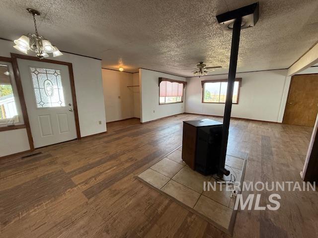 Foyer entrance with ceiling fan, a wood stove, a chandelier, dark wood-style flooring, and a textured ceiling