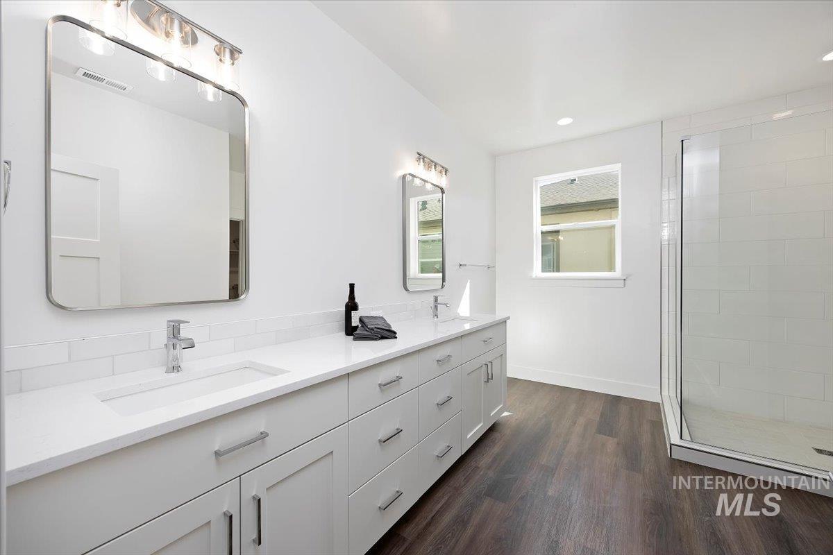 Bathroom featuring double vanity, a stall shower, dark wood-type flooring, and recessed lighting