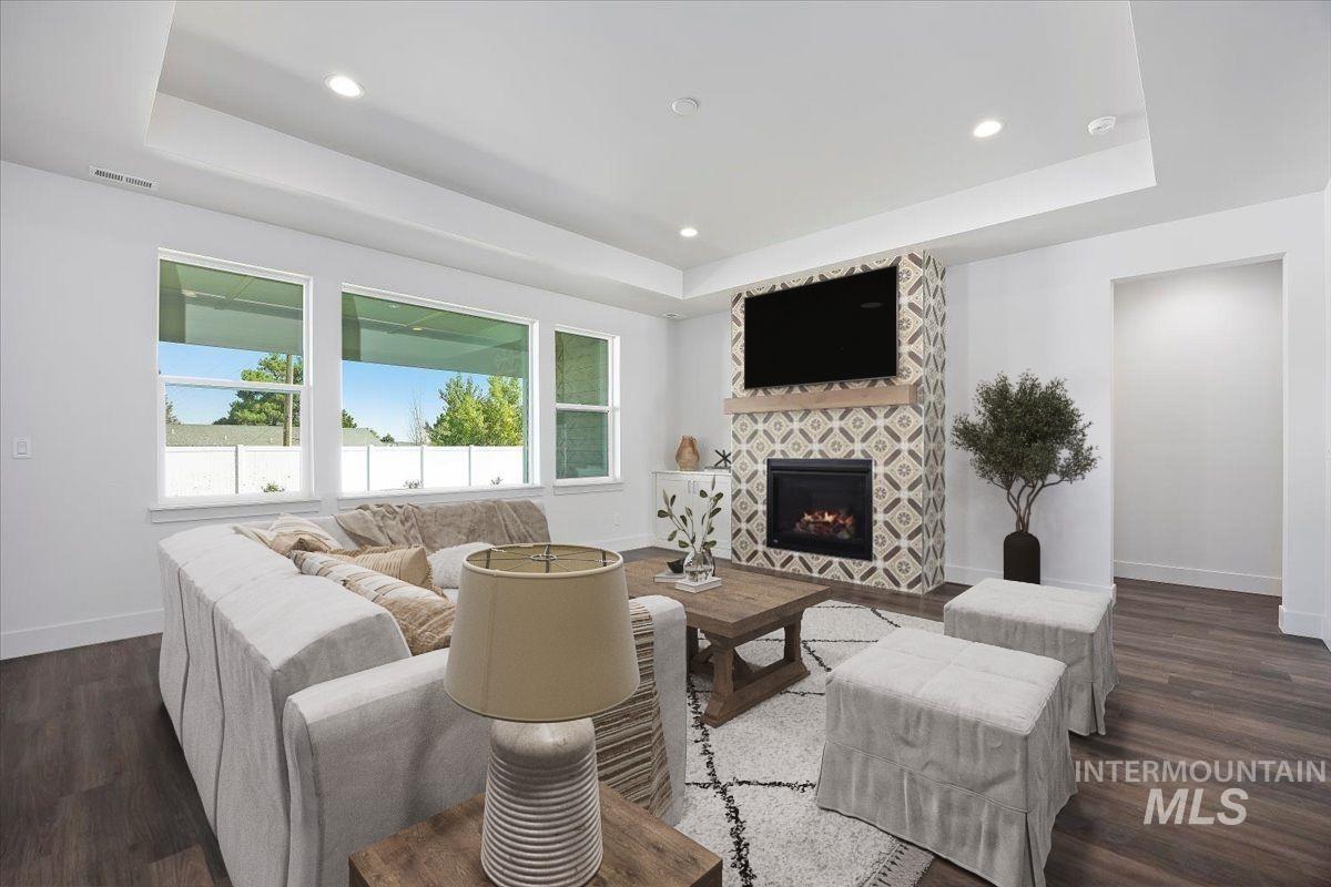Living room featuring a raised ceiling, dark wood-style flooring, a fireplace, and recessed lighting
