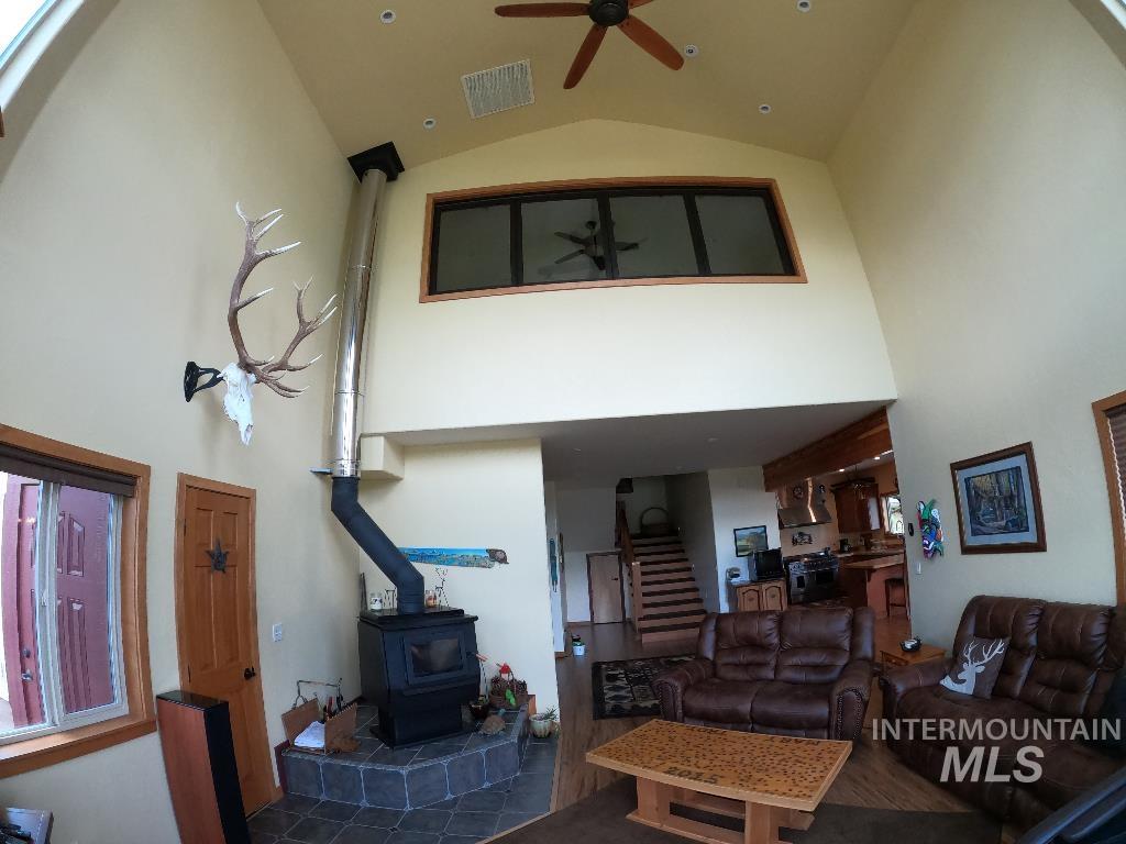 Living area featuring high vaulted ceiling, a wood stove, ceiling fan, and stairs