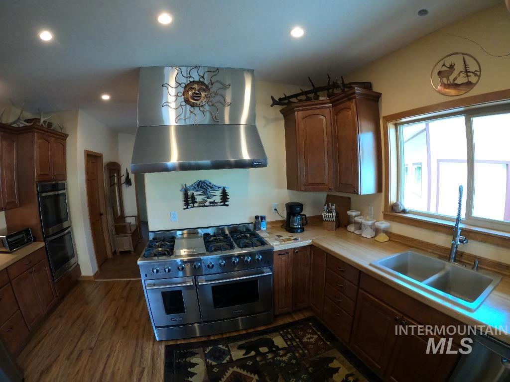 Kitchen featuring appliances with stainless steel finishes, light countertops, recessed lighting, dark wood-style floors, and wall chimney exhaust hood