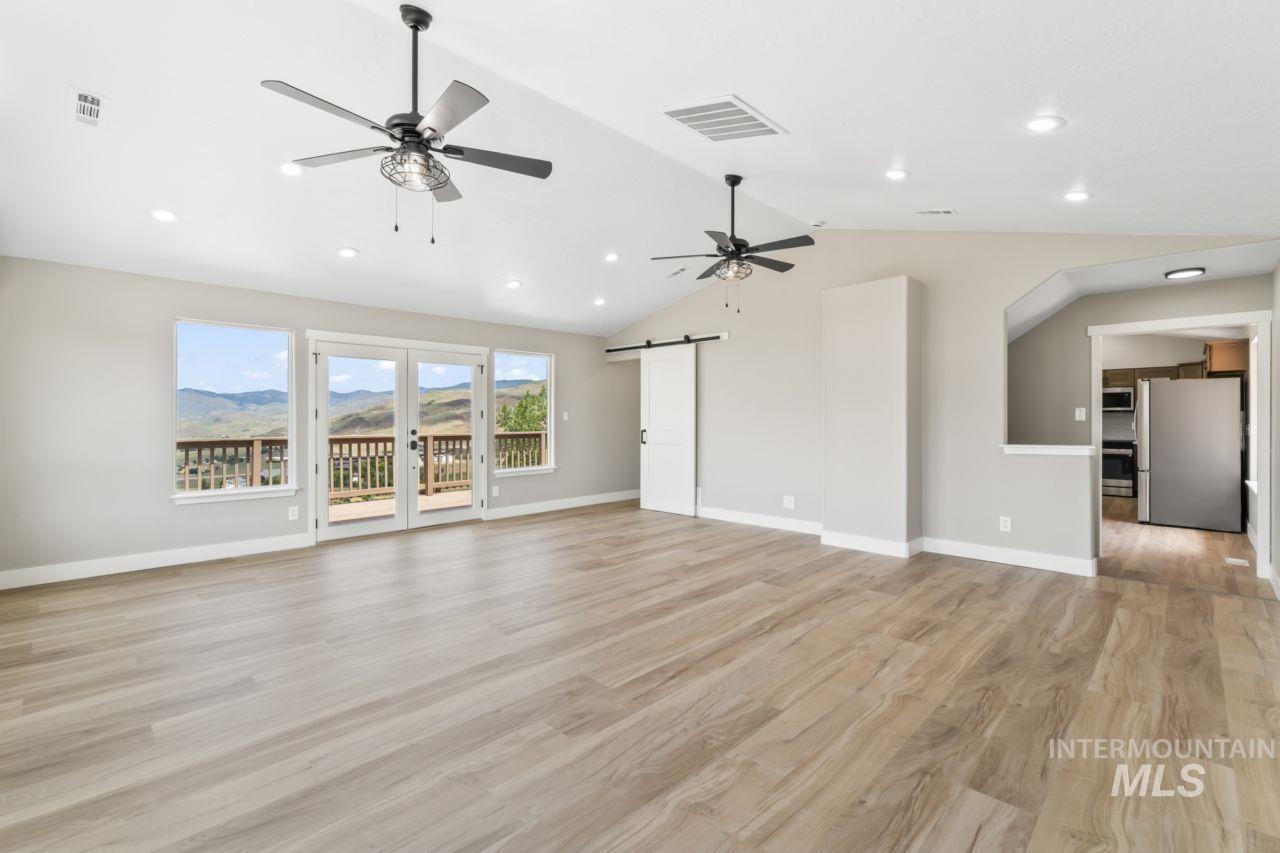 Unfurnished living room featuring a barn door, ceiling fan, lofted ceiling, light wood finished floors, and recessed lighting