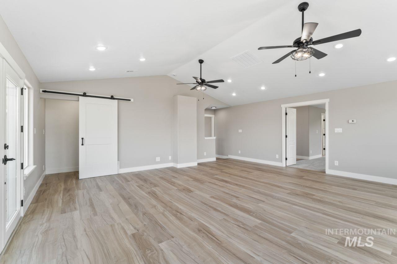 Unfurnished living room with a barn door, a ceiling fan, lofted ceiling, light wood finished floors, and recessed lighting