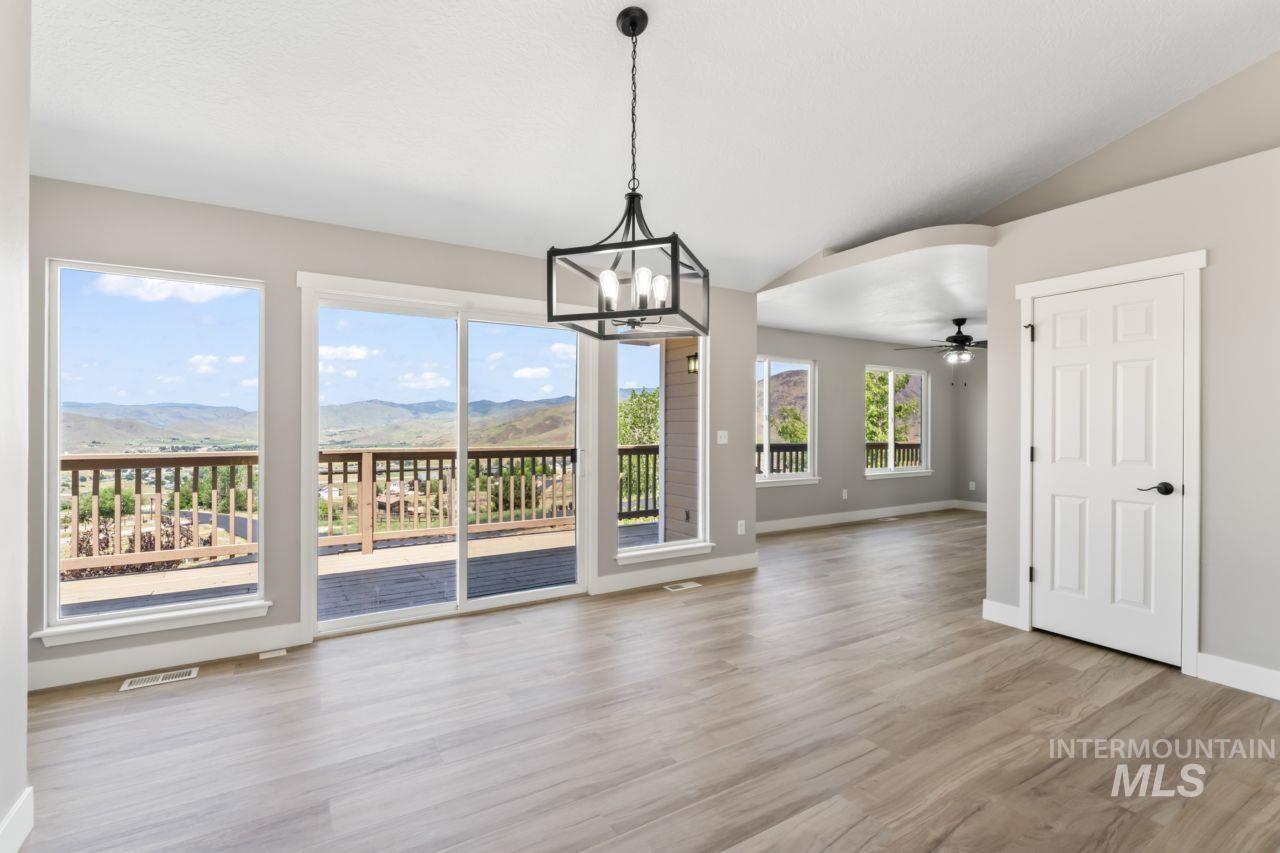Unfurnished dining area with a mountain view, a chandelier, wood finished floors, vaulted ceiling, and ceiling fan