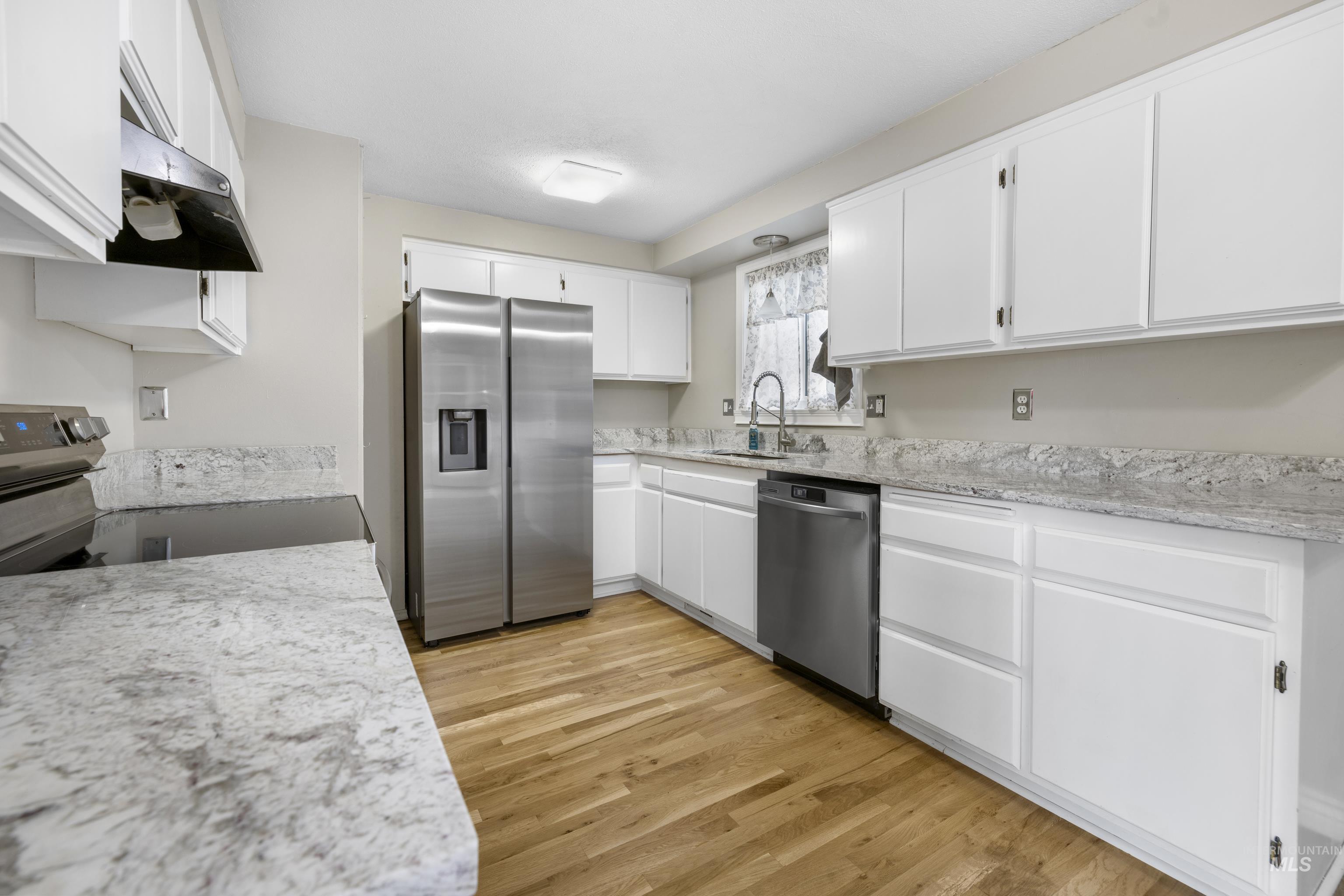 Kitchen with appliances with stainless steel finishes, ventilation hood, white cabinets, and light wood-style flooring