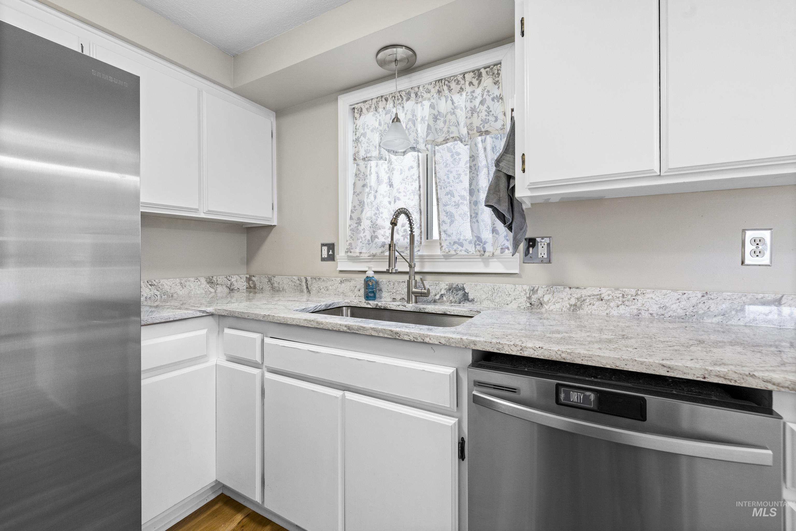 Kitchen featuring stainless steel appliances, white cabinets, and light stone countertops