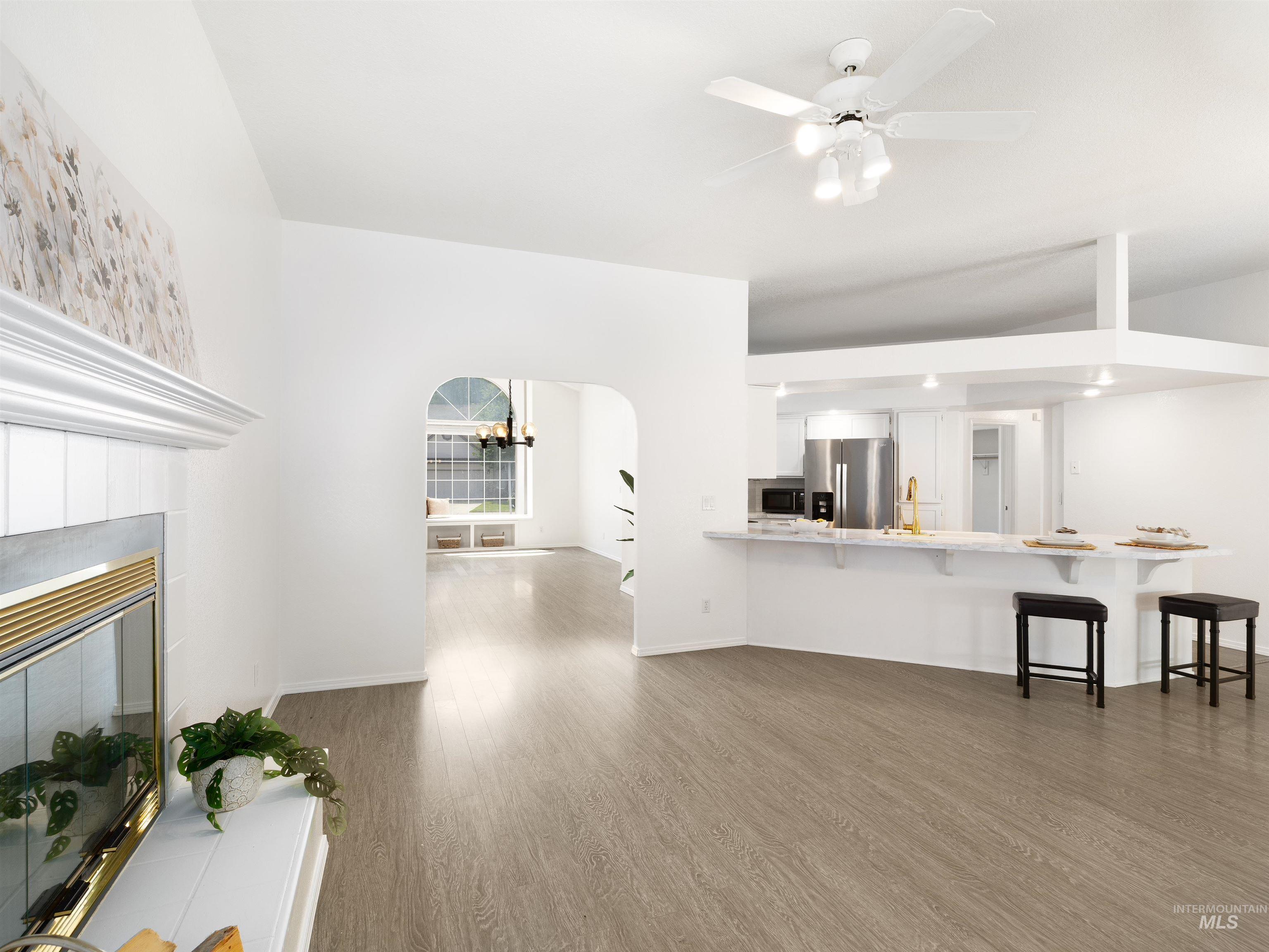 Unfurnished living room with wood finished floors, a fireplace, a ceiling fan, and arched walkways
