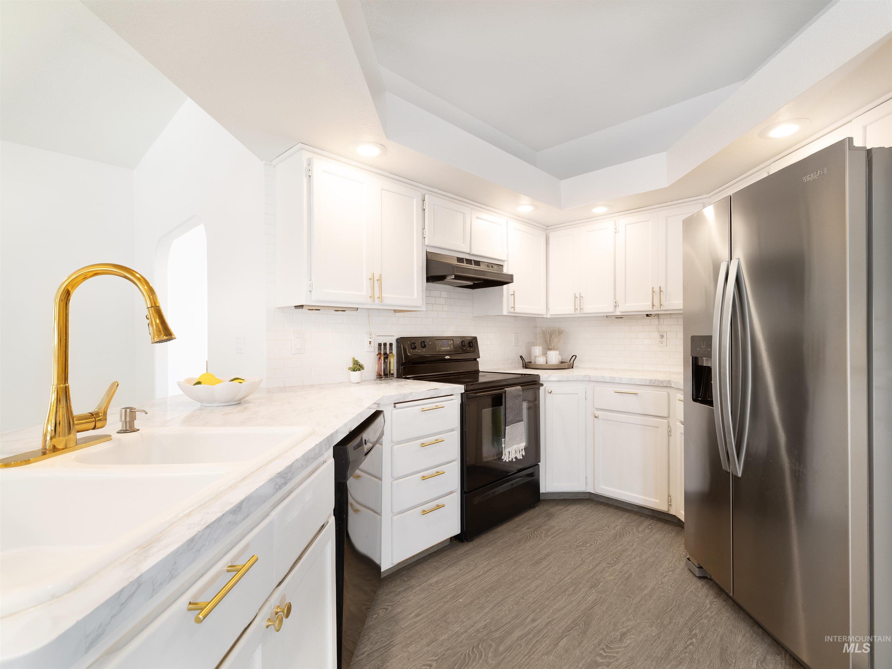 Kitchen featuring black appliances, dark wood-style flooring, white cabinets, a raised ceiling, and light countertops