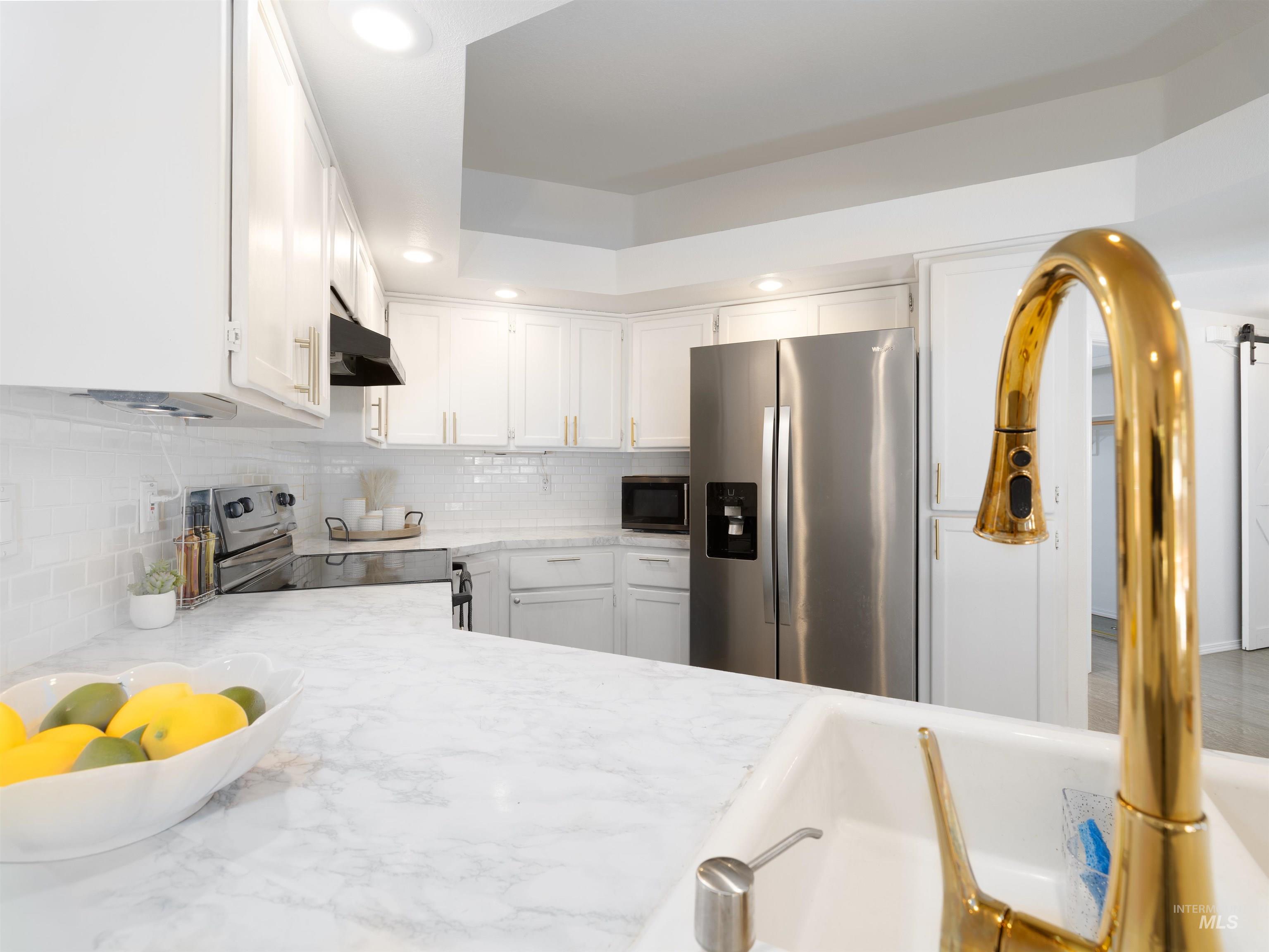 Kitchen featuring stainless steel appliances, recessed lighting, white cabinetry, decorative backsplash, and under cabinet range hood