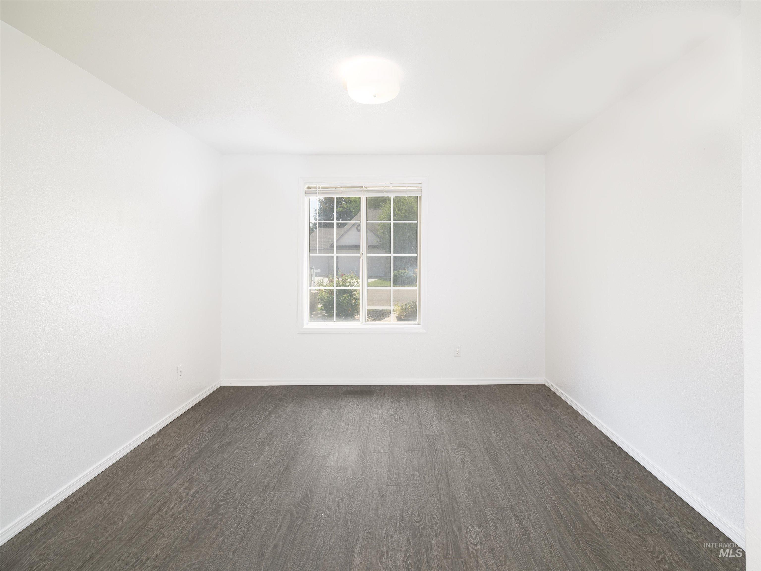 Empty room with dark wood-type flooring and baseboards