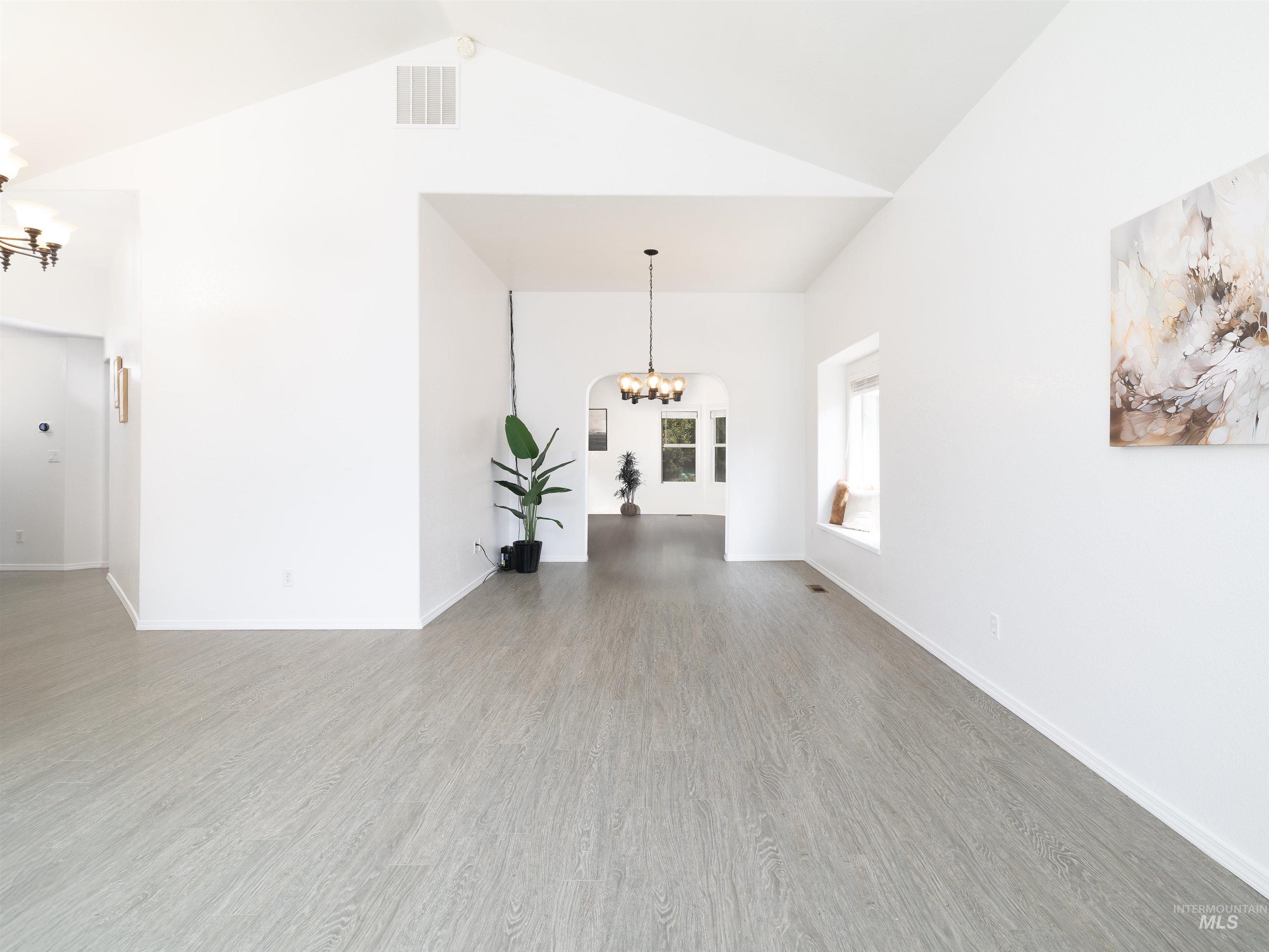 Unfurnished living room with a chandelier, wood finished floors, and high vaulted ceiling
