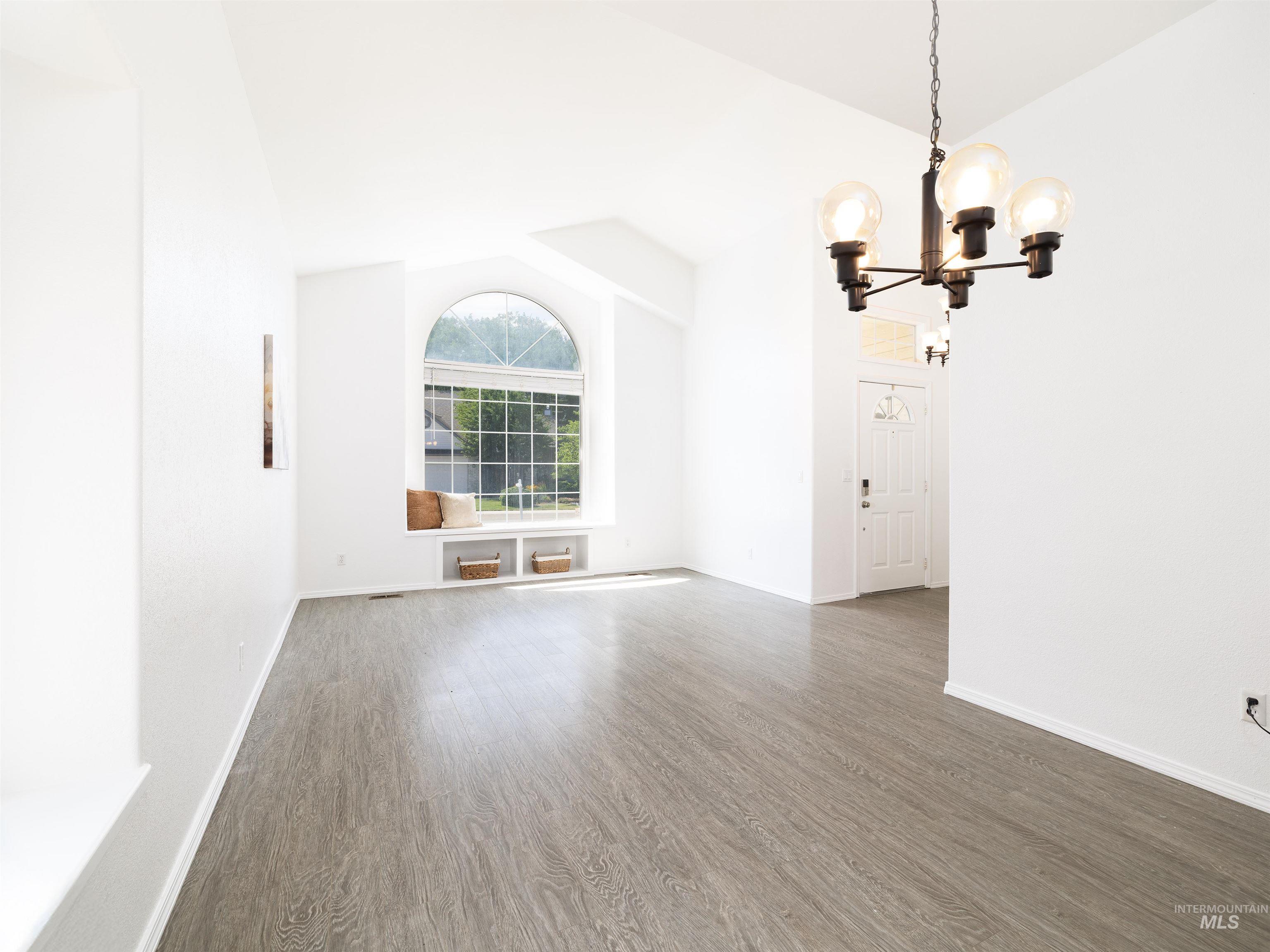 Unfurnished living room with lofted ceiling, wood finished floors, and a chandelier