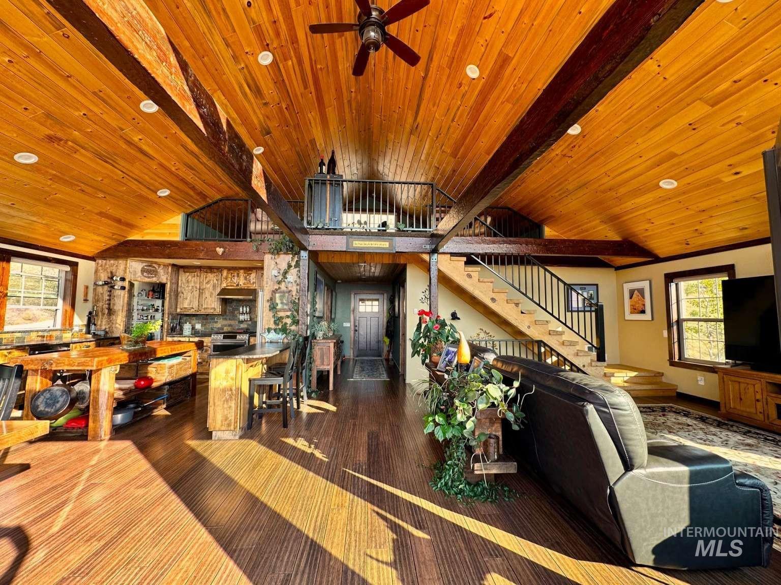Living room featuring stairs, dark wood-style flooring, a wooden ceiling with exposed beams, ceiling fan, and high vaulted ceiling