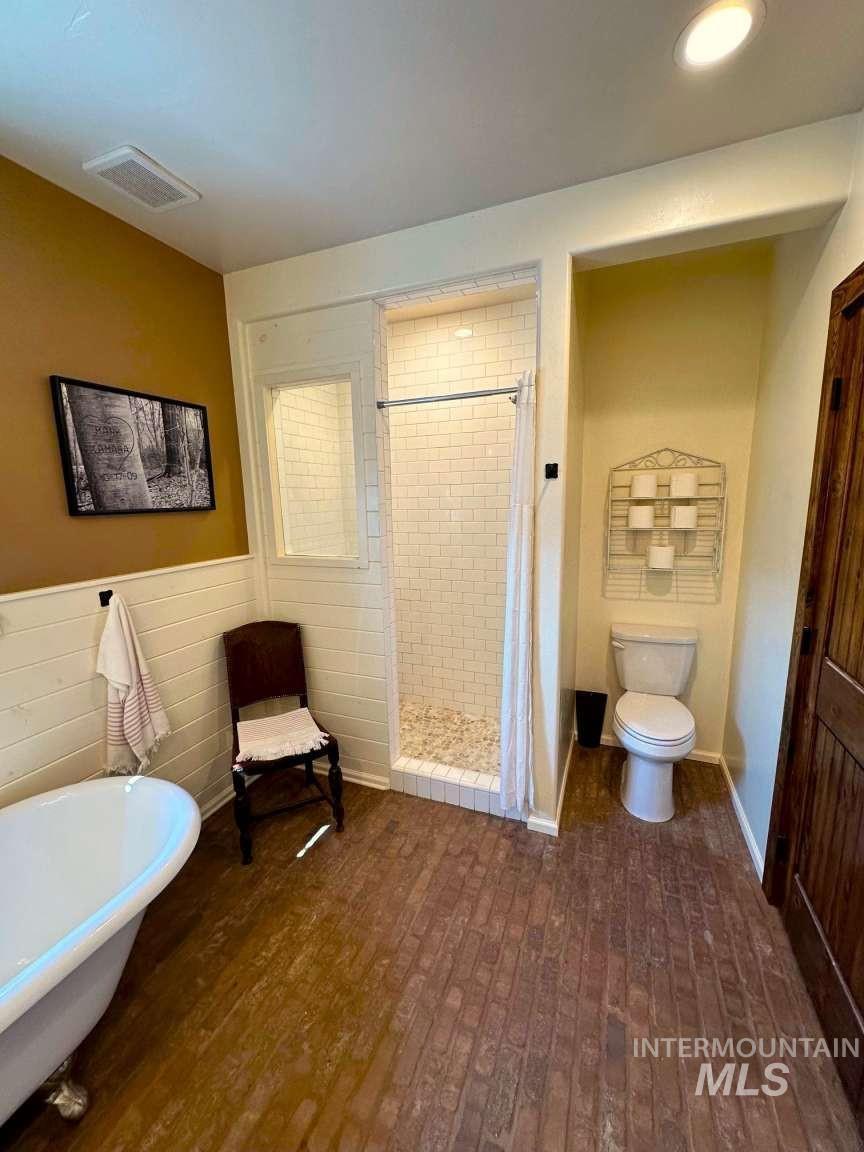 Full bath with a shower stall, a freestanding bath, and dark wood-style floors