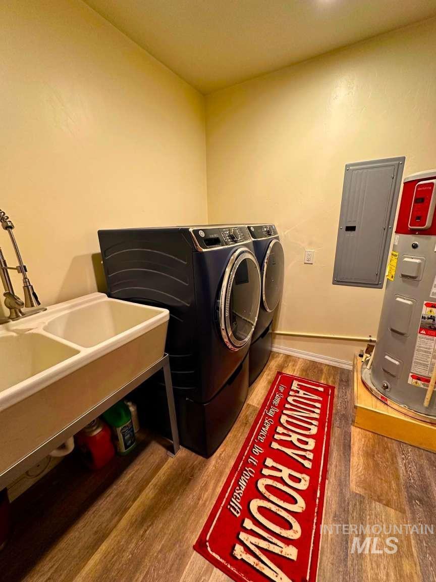 Laundry area featuring light wood finished floors, electric panel, washing machine and dryer, and water heater