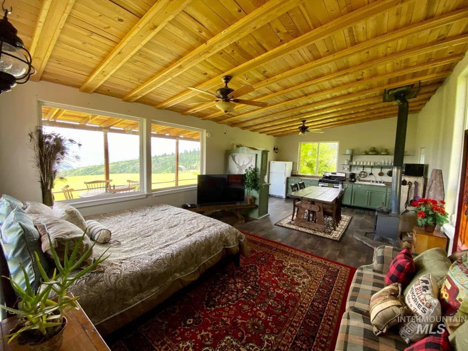 Bedroom with a wood stove, freestanding refrigerator, wood ceiling, and dark wood-style flooring