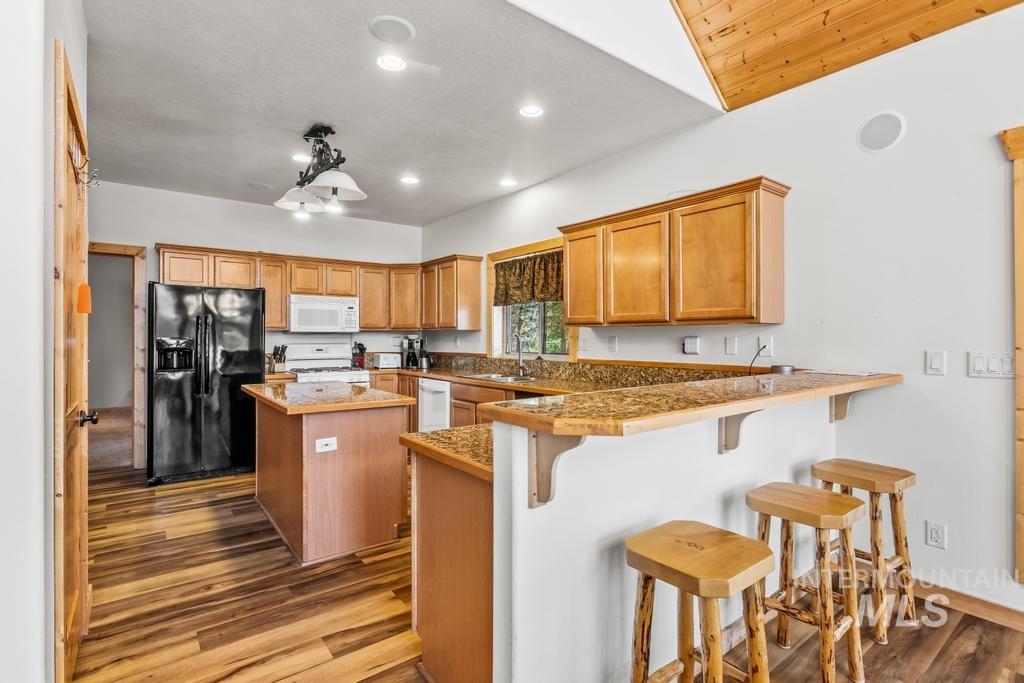 Kitchen featuring white appliances, a kitchen bar, a kitchen island, a peninsula, and brown cabinets