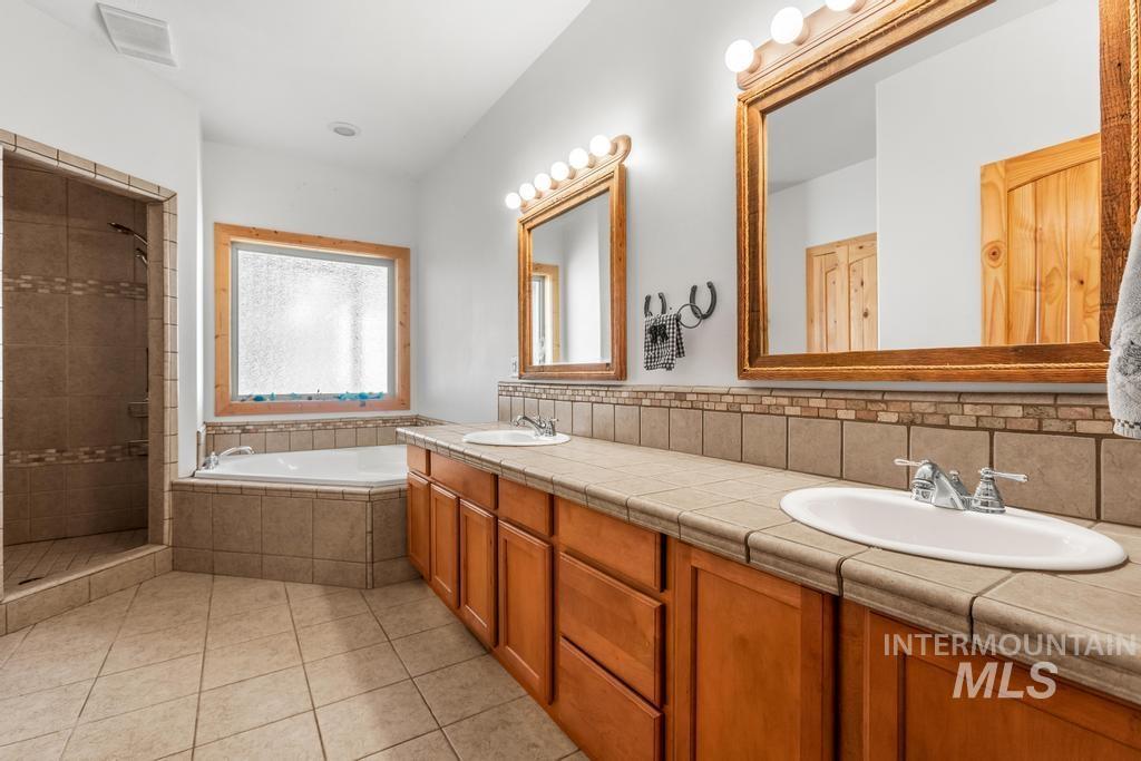 Bathroom featuring double vanity, a bath, light tile patterned floors, and a tile shower