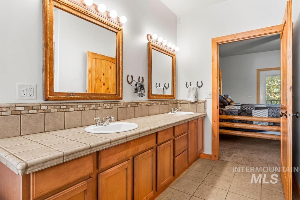 Ensuite bathroom featuring double vanity, light tile patterned floors, and backsplash