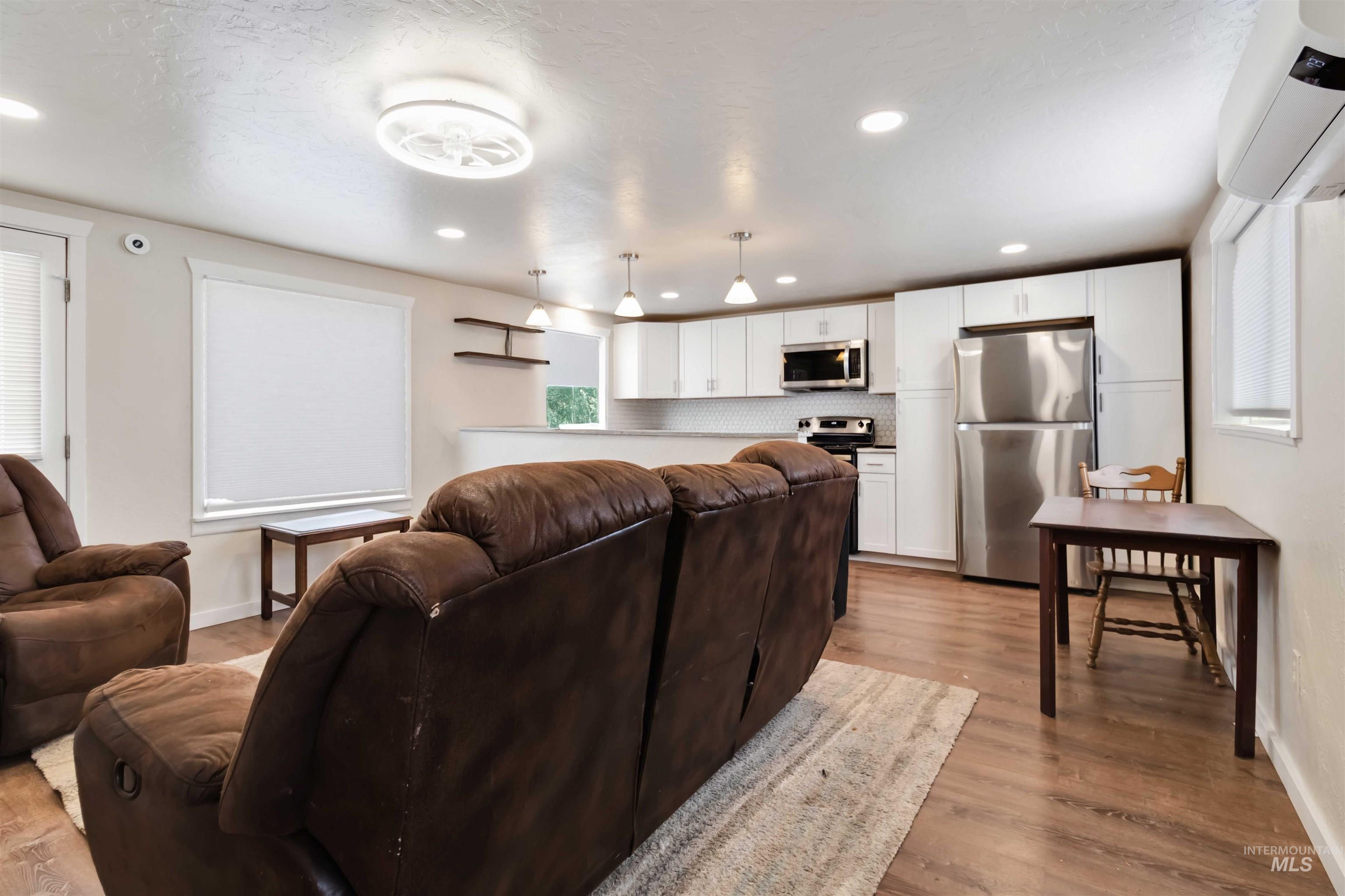 Living room featuring light wood-type flooring, healthy amount of natural light, an AC wall unit, recessed lighting, and a textured ceiling