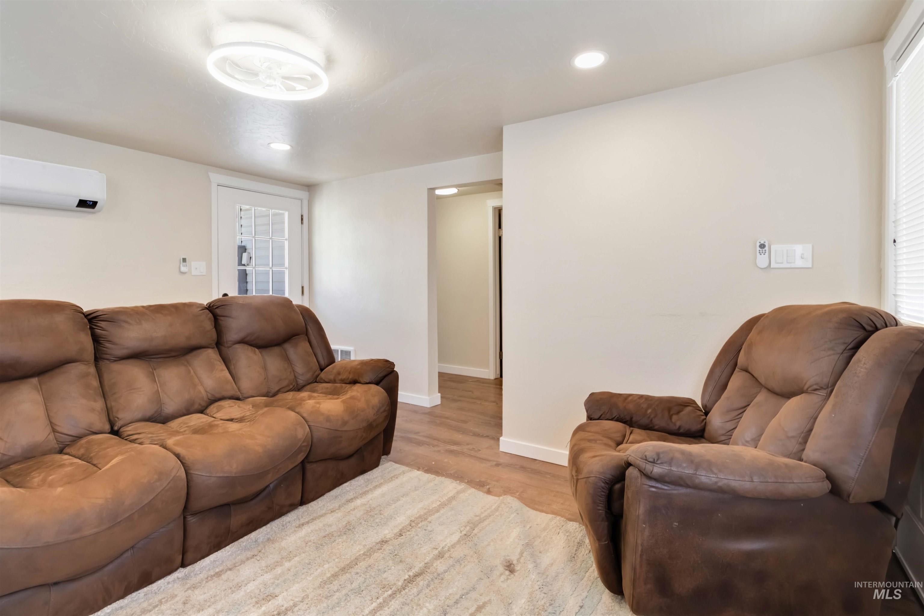 Living area with light wood finished floors, recessed lighting, and a wall unit AC