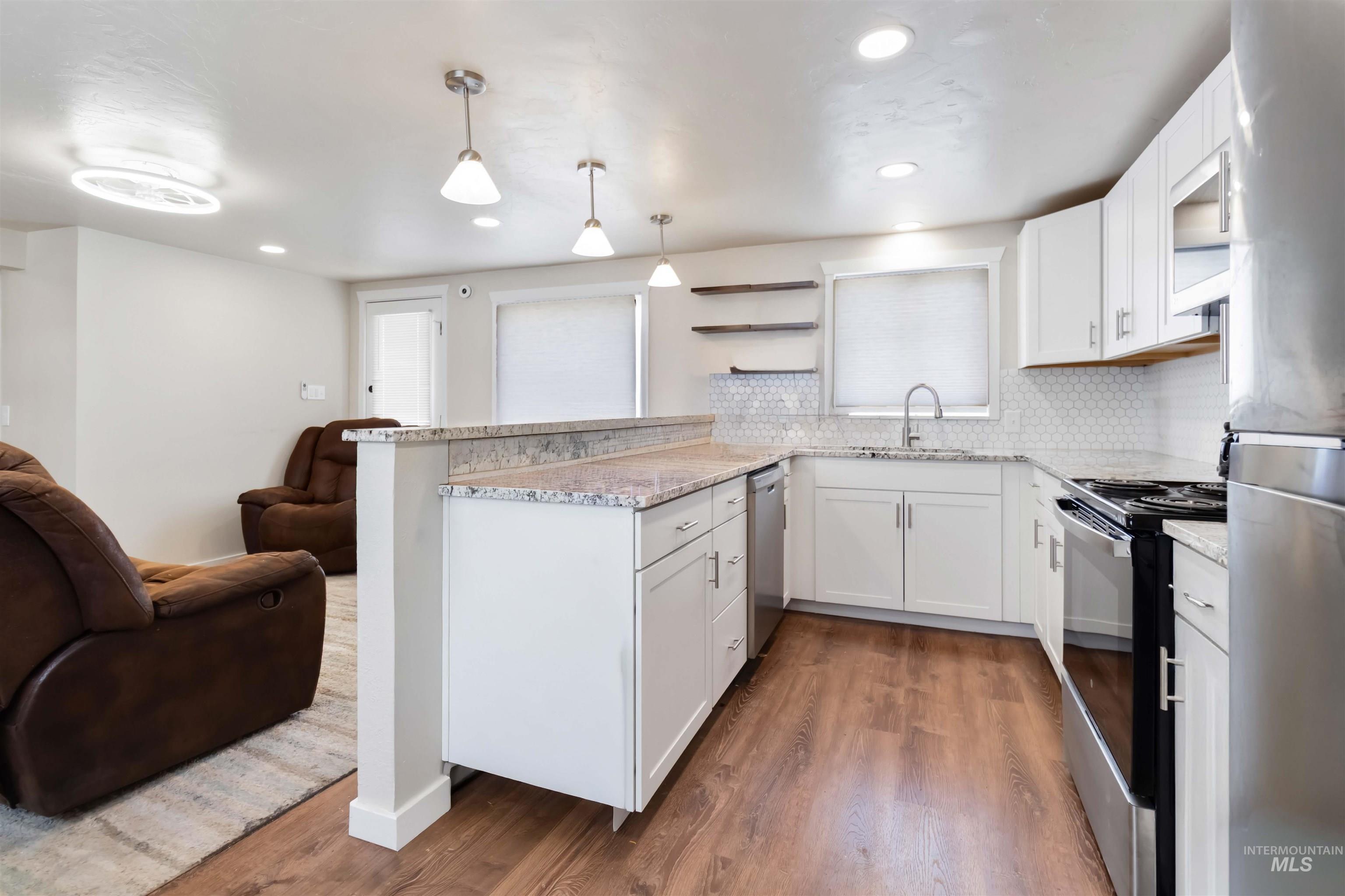 Kitchen with a peninsula, stainless steel appliances, white cabinets, dark wood-style flooring, and hanging light fixtures