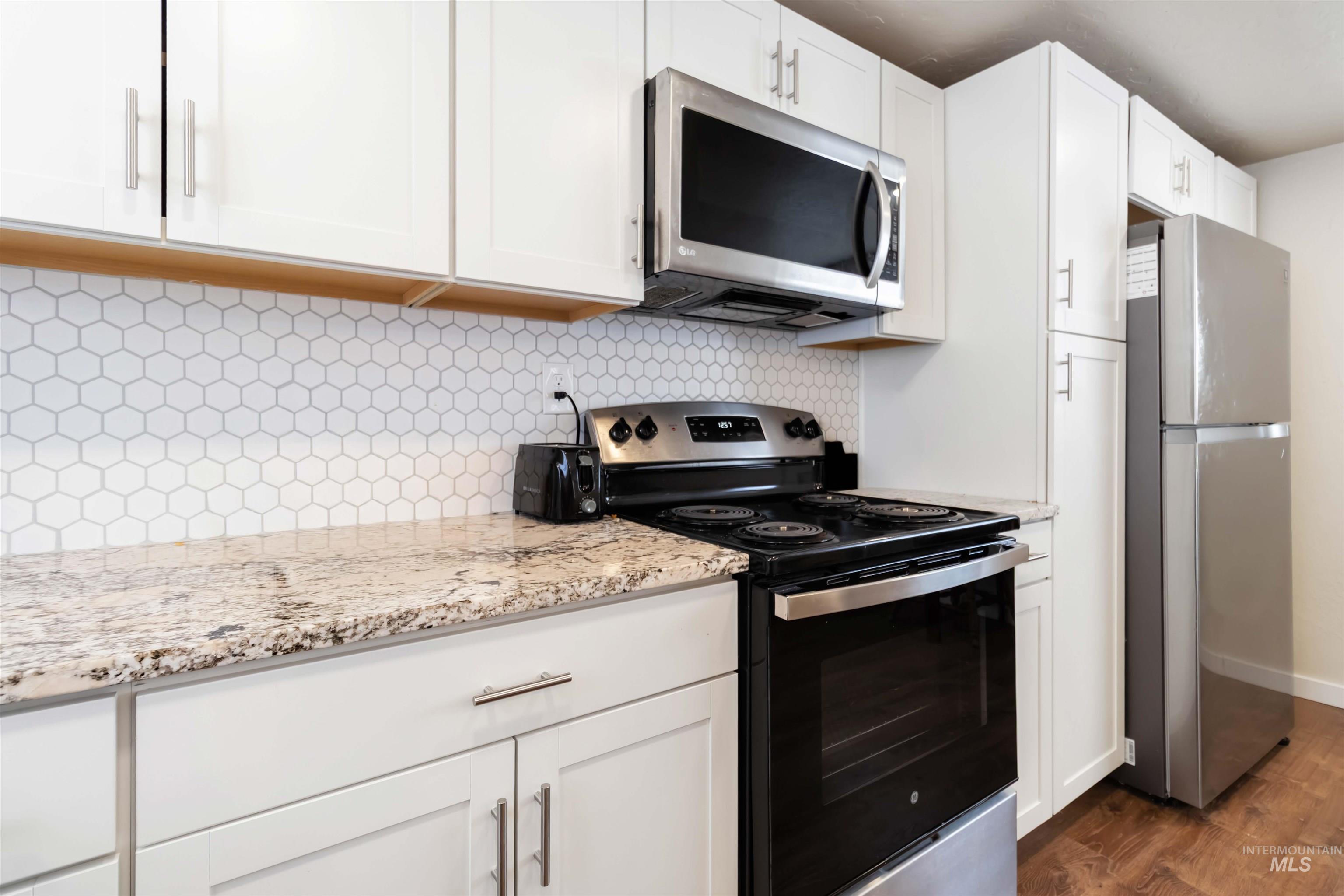 Kitchen with stainless steel appliances, tasteful backsplash, light stone counters, and white cabinets