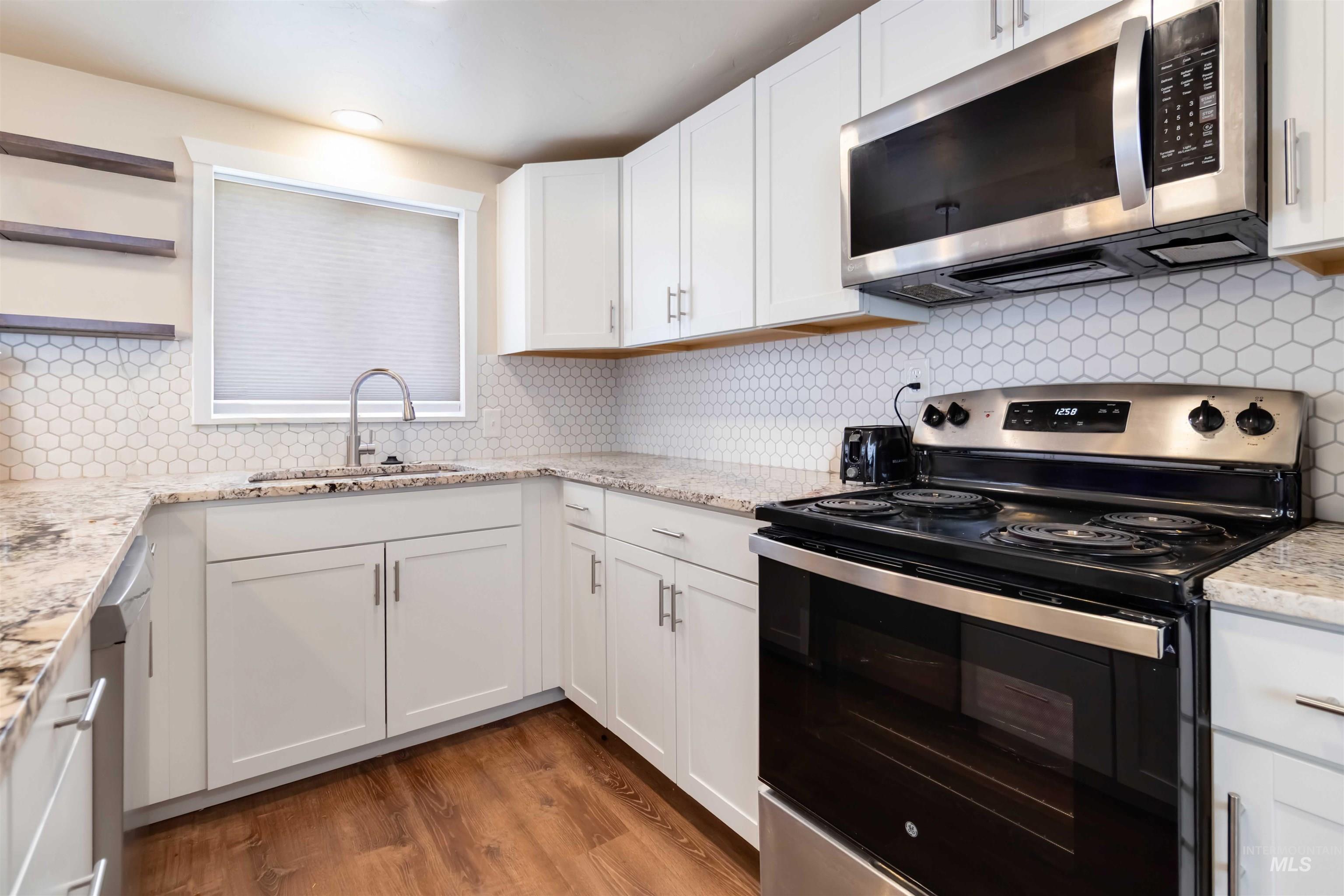 Kitchen featuring appliances with stainless steel finishes, tasteful backsplash, white cabinets, light stone counters, and light wood-type flooring