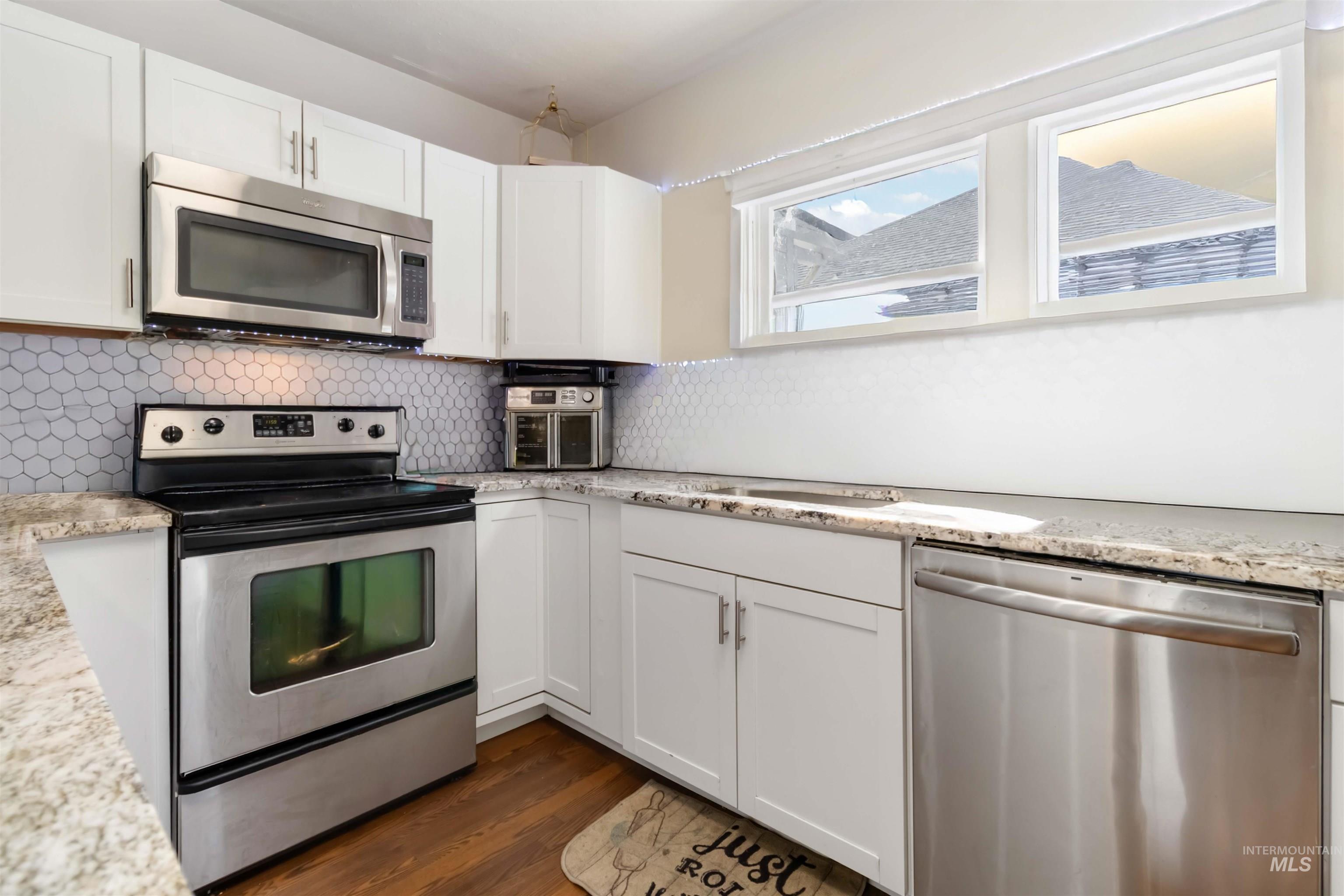 Kitchen featuring appliances with stainless steel finishes, white cabinets, tasteful backsplash, and light stone countertops