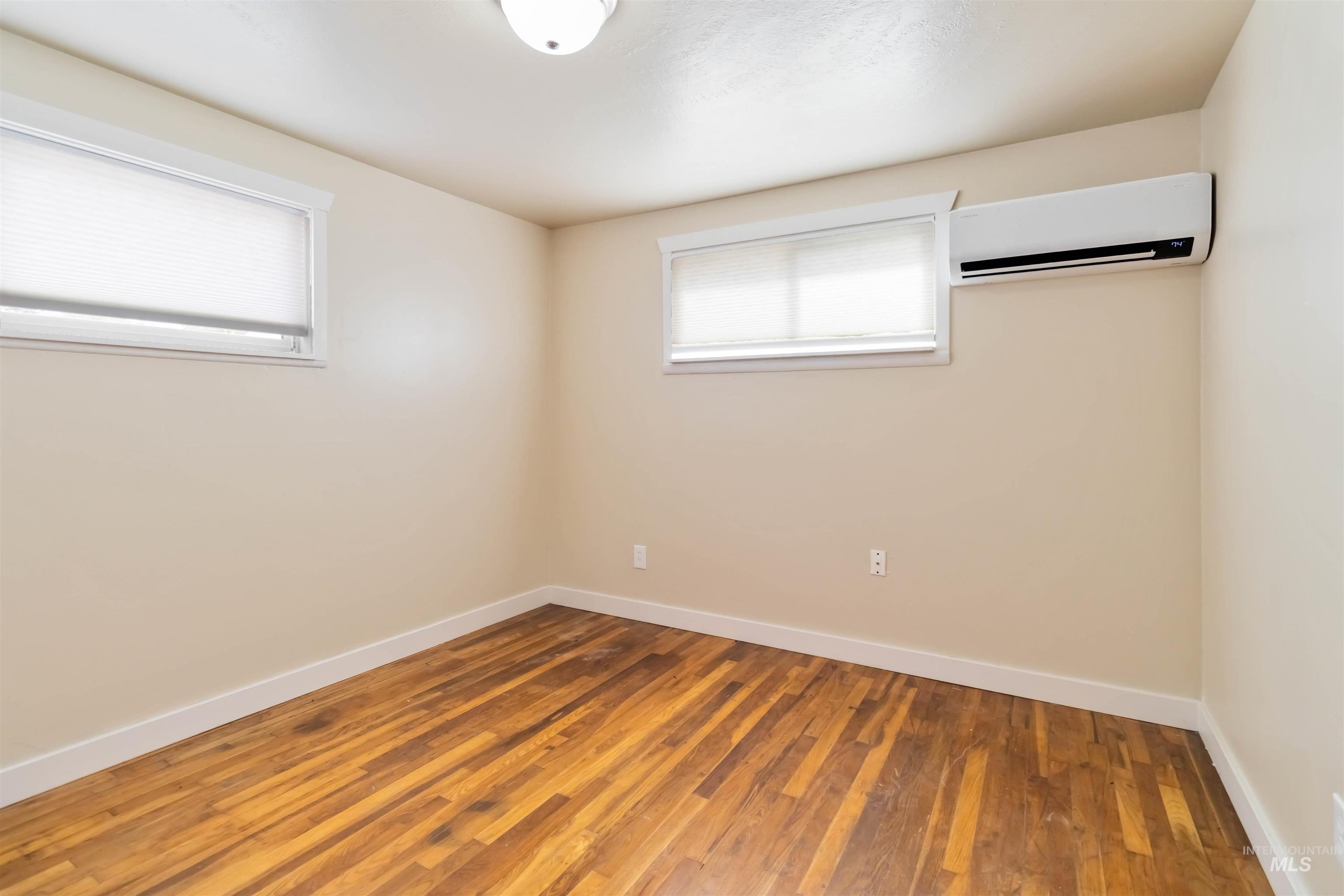 Empty room featuring a wall unit AC and wood finished floors