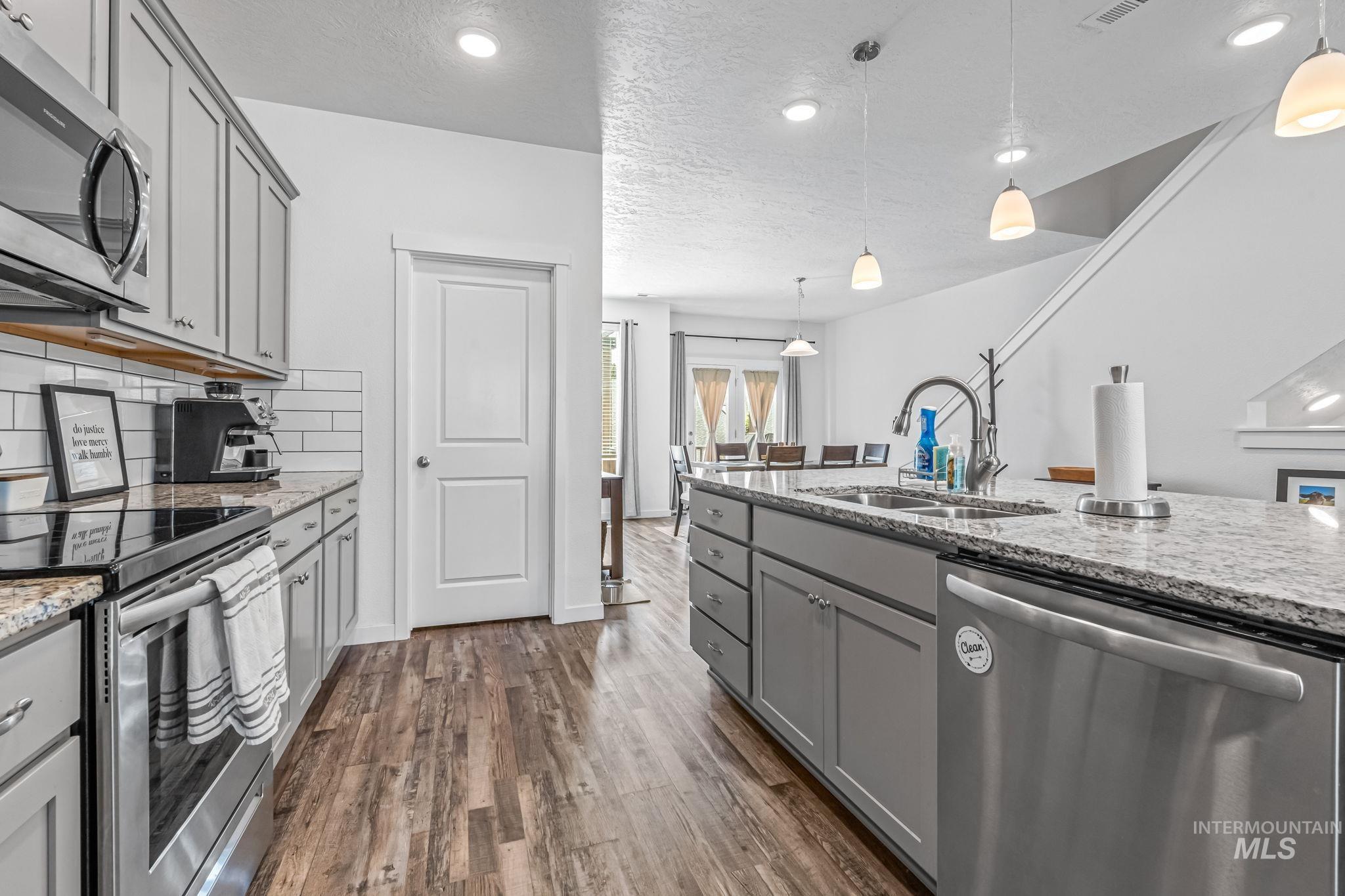 Kitchen featuring stainless steel appliances, gray cabinets, dark wood-style flooring, light stone counters, and tasteful backsplash