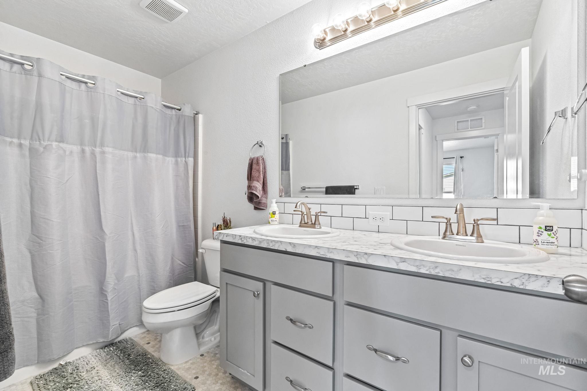 Full bath featuring double vanity, decorative backsplash, curtained shower, and tile patterned flooring