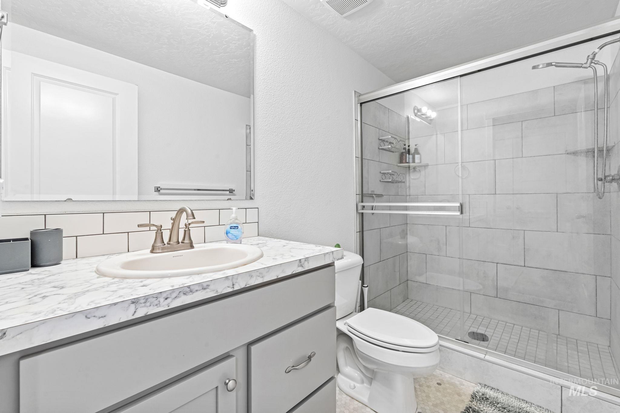 Bathroom featuring vanity, a stall shower, a textured ceiling, and backsplash