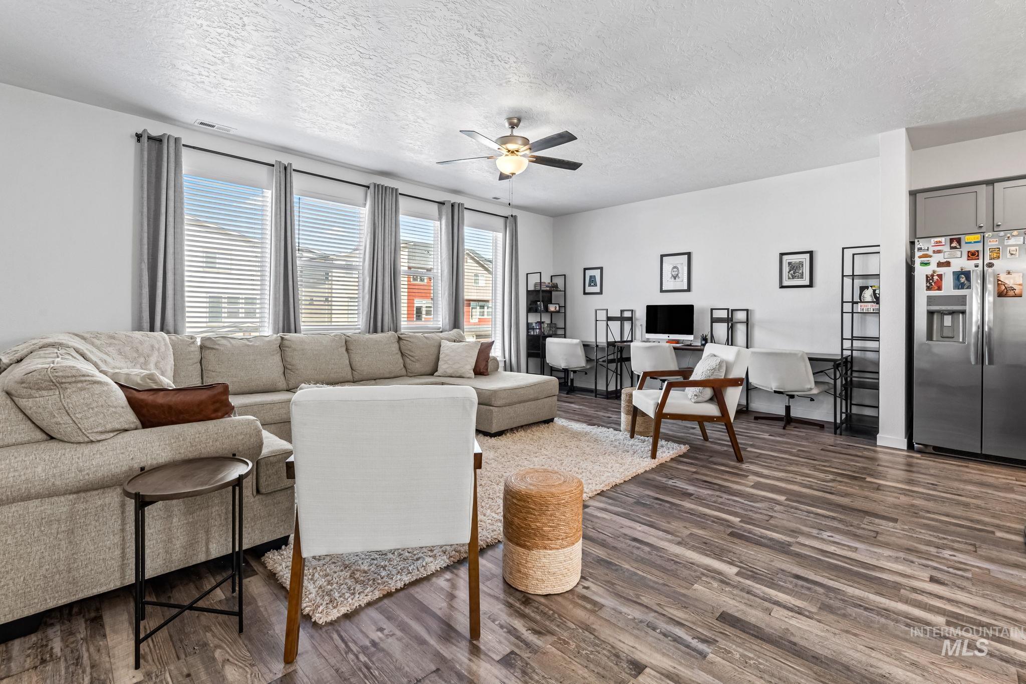 Living room with a ceiling fan, a textured ceiling, and dark wood-style floors