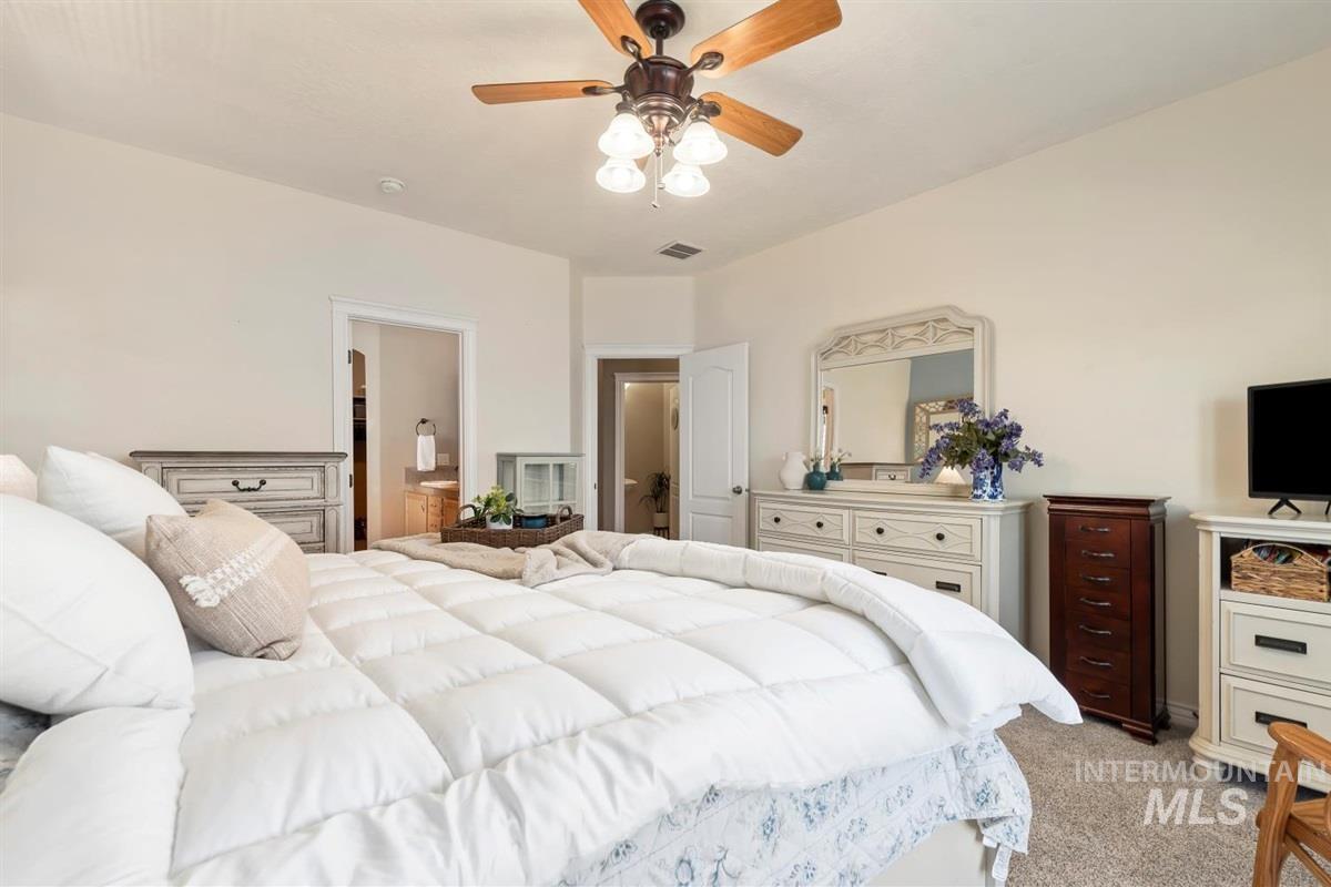 Bedroom with light carpet, ceiling fan, and connected bathroom
