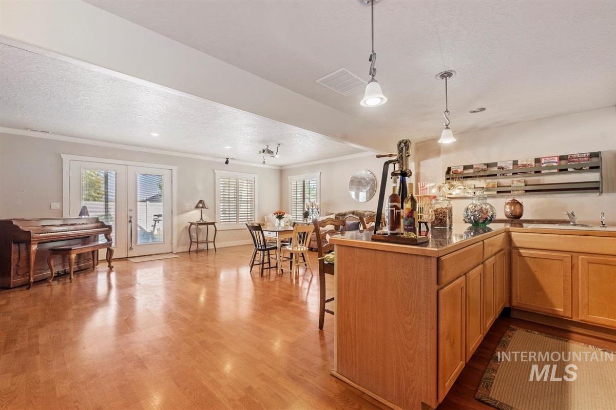 Recreation room featuring ornamental molding, wood finished floors, healthy amount of natural light, a textured ceiling, and pendant lighting