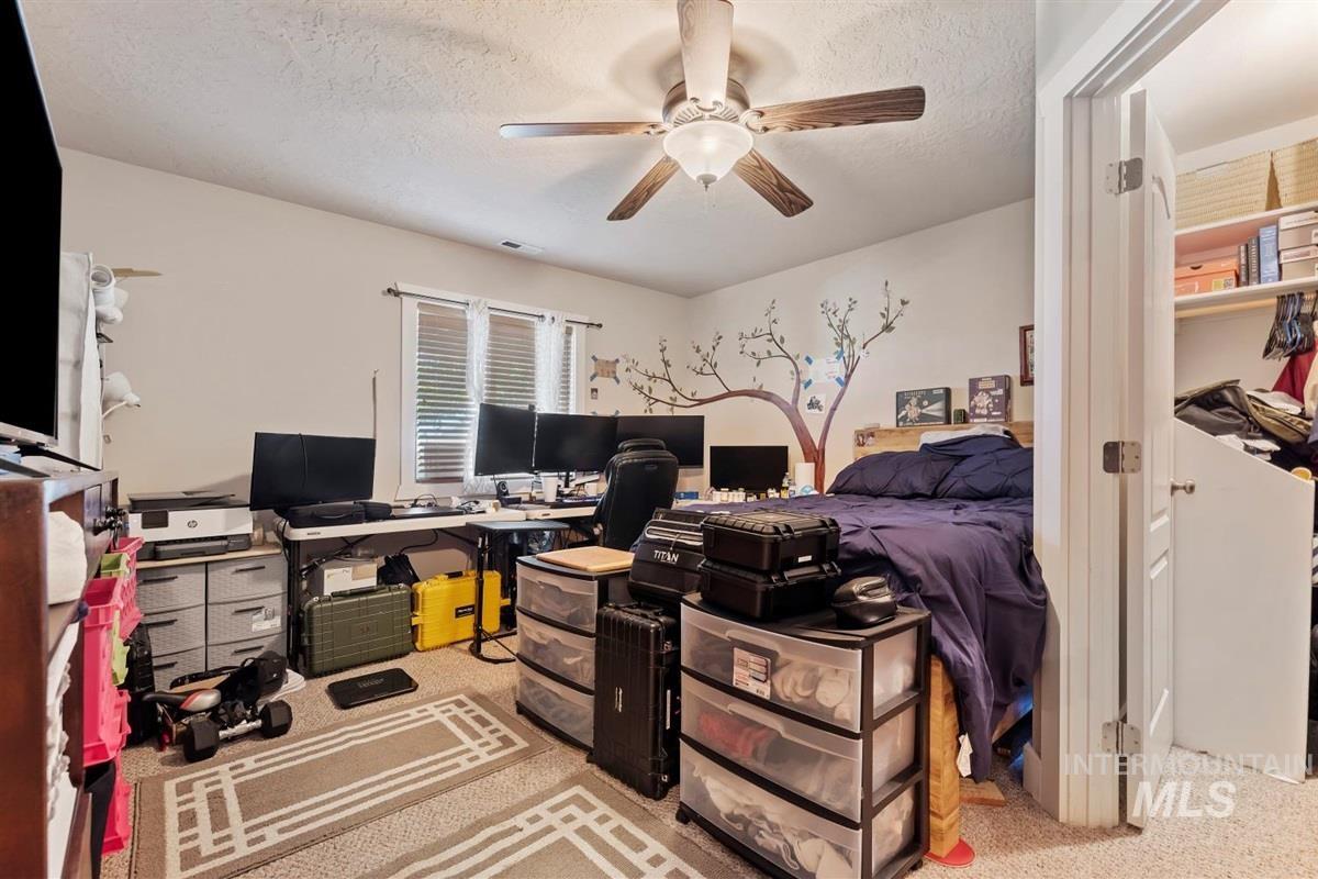Carpeted bedroom featuring a desk, a textured ceiling, and a ceiling fan