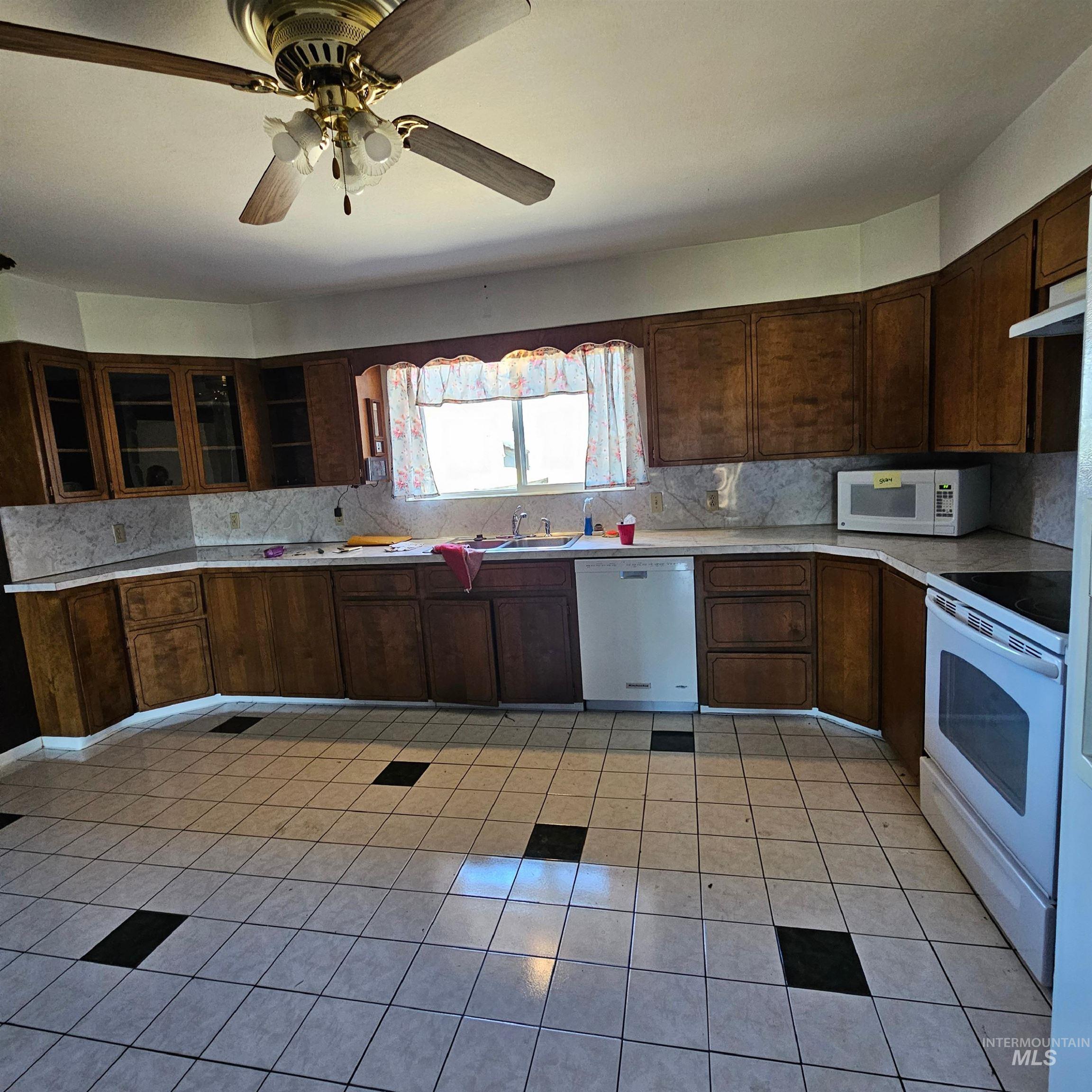 Kitchen with light countertops, light tile patterned floors, white appliances, dark brown cabinetry, and tasteful backsplash