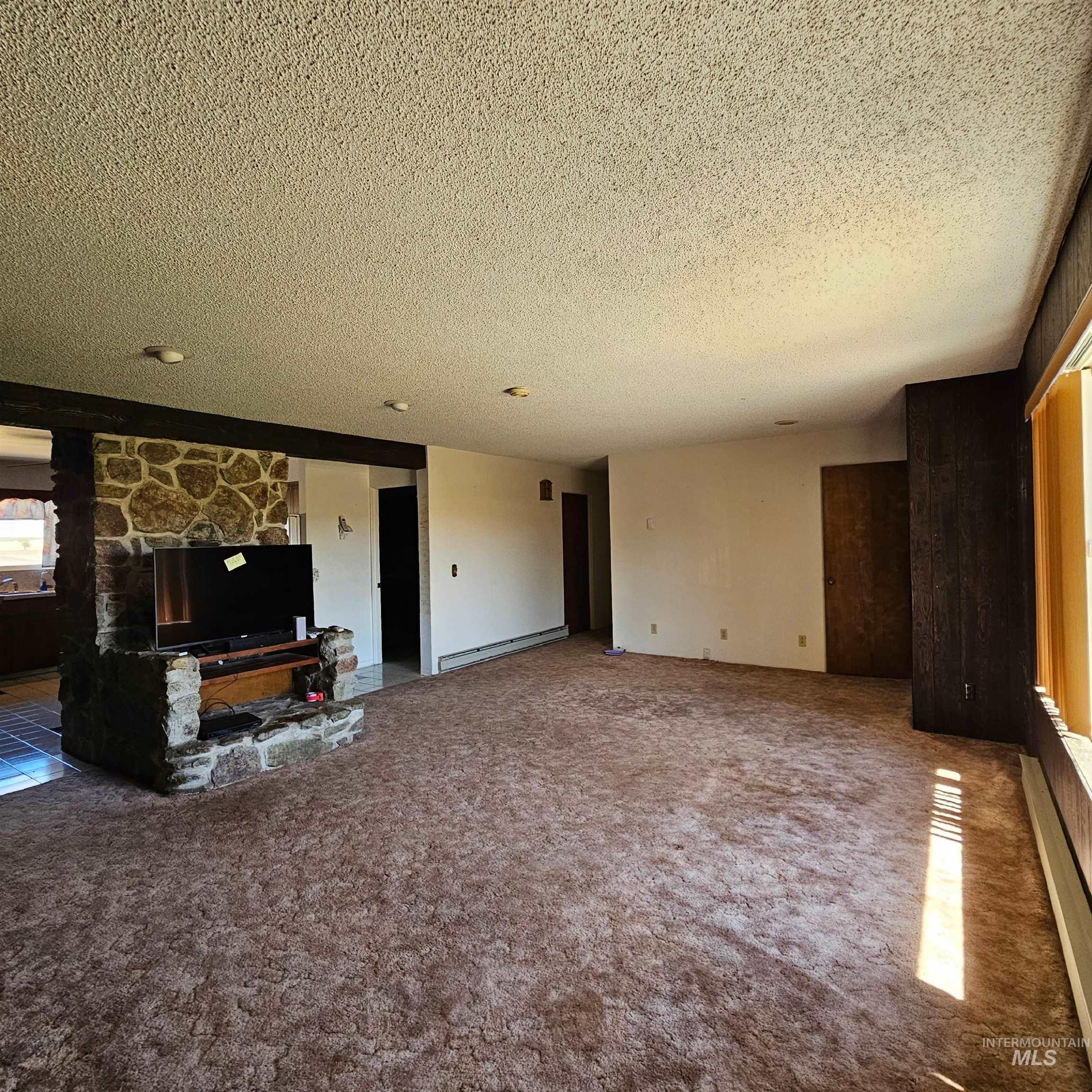 Unfurnished living room with carpet floors, a textured ceiling, baseboard heating, a fireplace, and a baseboard heating unit