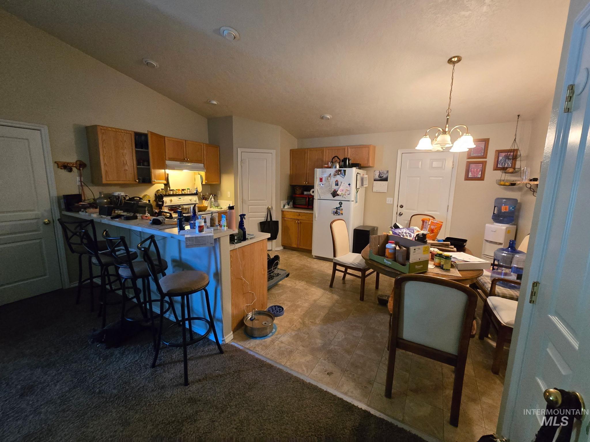 Kitchen featuring freestanding refrigerator, a peninsula, brown cabinets, a kitchen breakfast bar, and lofted ceiling