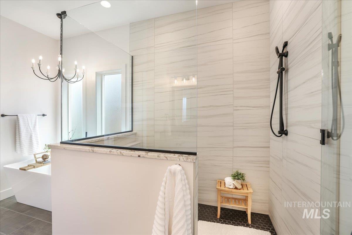 Full bath featuring walk in shower, a freestanding bath, a chandelier, and tile patterned floors