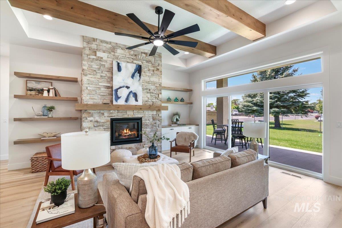 Living room featuring beamed ceiling, light wood-style flooring, a towering ceiling, a stone fireplace, and a ceiling fan